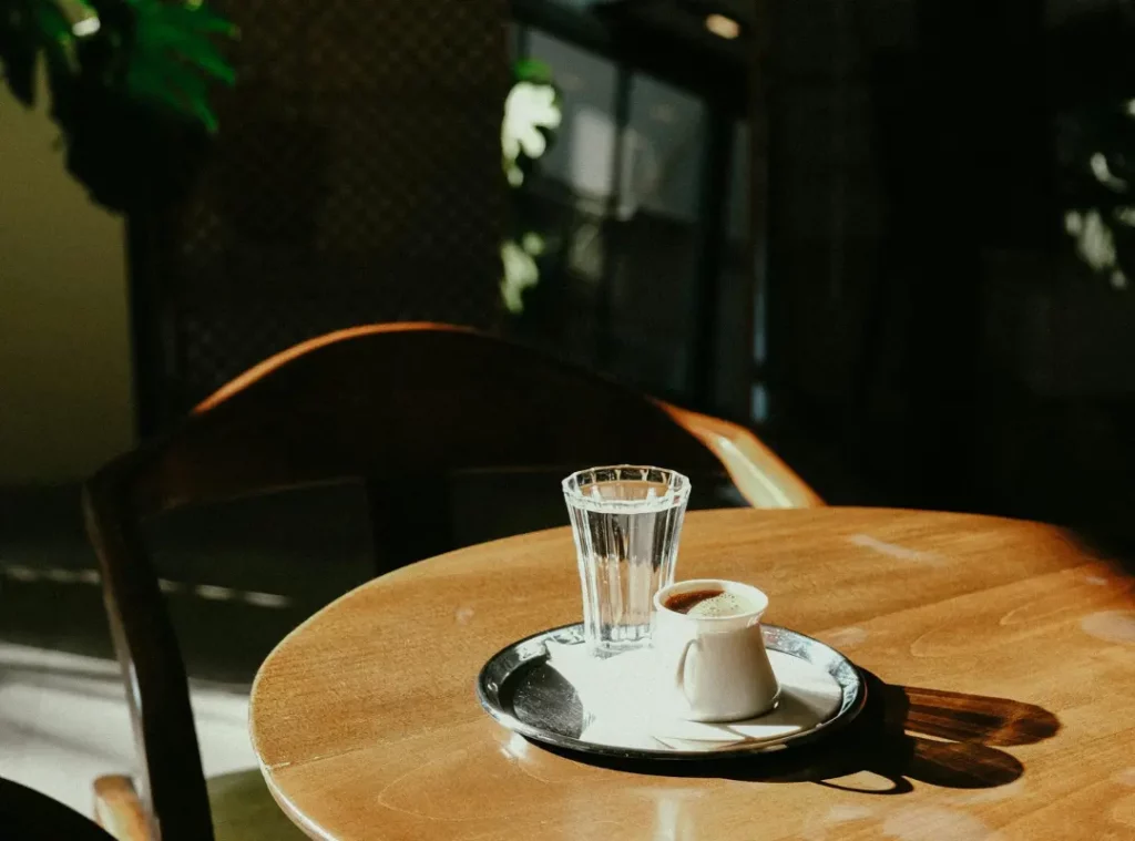 แก้วน้ำและกาแฟเสิร์ฟบนโต๊ะไม้ทรงกลมในมุมคาเฟ่โทนเข้ม บรรยากาศเงียบสงบและอบอุ่น